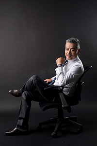 黑色商务背景摄影照片_坐在椅子上的成功商务男士