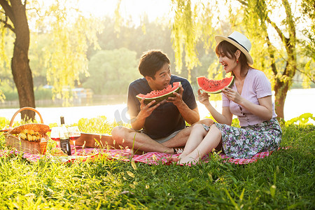 青年伴侣吃西瓜摄影照片_在公园里郊游的幸福情侣