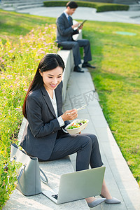 白领吃饭摄影照片_商务女性坐着户外边吃饭边工作