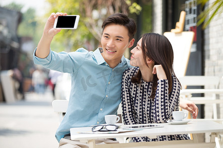 数码消费摄影照片_青年情侣坐在咖啡馆里用手机自拍