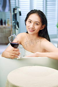 洗澡泡澡摄影照片_浴缸内漂亮的年轻女人和红酒