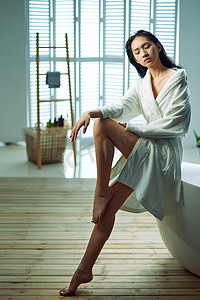 美女浴缸洗澡摄影照片_身穿浴袍的青年女人坐在浴缸边