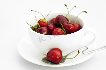 堆积的物品摄影照片_白底上的杯子茶碟勺子樱桃和草莓