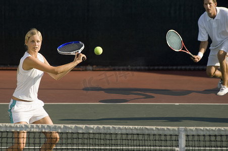 年轻女子网球运动员与双打搭档在背景中击球