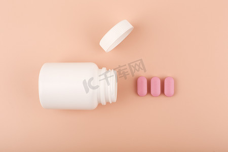 药丸药瓶摄影照片_白色打开药瓶，粉红色溢出的药丸在柔和的背景下排成一排