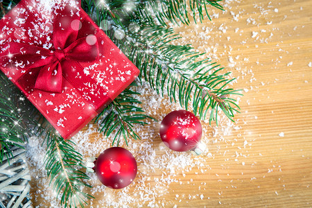 松枝装饰摄影照片_木头上有松枝、红色圣诞球和雪的礼盒