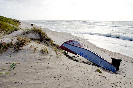 生锈的船躺在海沙丘海滩上，人们走路