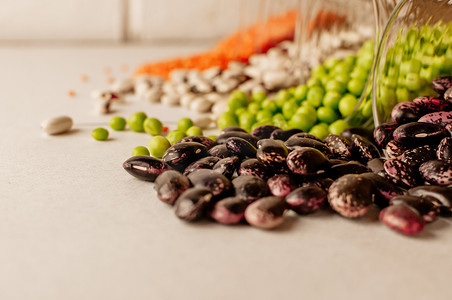 一组不同的干豆类放在玻璃杯中，有点散落：红扁豆、绿豌豆、红豆、白豆。
