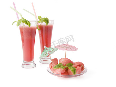 奶昔西瓜汁摄影照片_两杯西瓜饮料（冰沙）和一个用薄荷叶和雨伞装饰的球形西瓜。