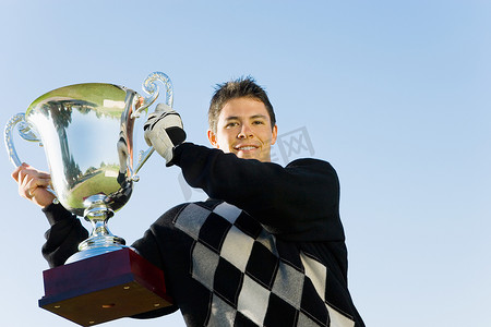 高尔夫球奖杯摄影照片_在晴朗的天空下拿着奖杯的快乐年轻人的画像