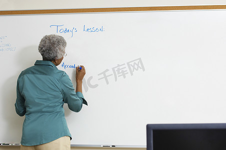 卷发背面摄影照片_教室里一位资深教师在白板上写字的背面视角
