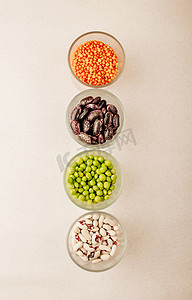 干豆类摄影照片_玻璃杯中各种干豆类的集合，垂直排列的绿豌豆、红扁豆、红豆、白豆在白色背景中特写