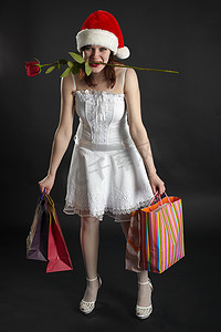 圣诞衣服摄影照片_戴着圣诞帽的有趣女孩，带着购物和玫瑰