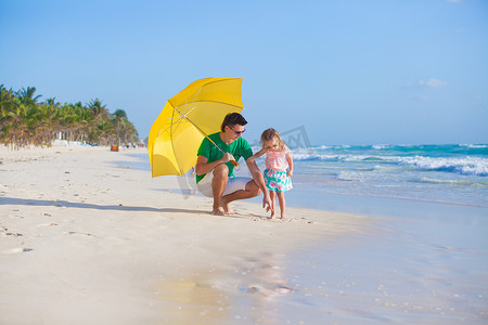 阳光明媚的日子里，年轻的父亲和他可爱的小女儿躲在一把黄色的雨伞下