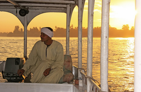 三桅小帆船摄影照片_日落时分，埃及船长在尼罗河上驾驶他的船，L