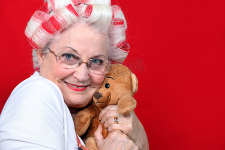 一位拿着卷发器的老妇人抱着一只泰迪熊。