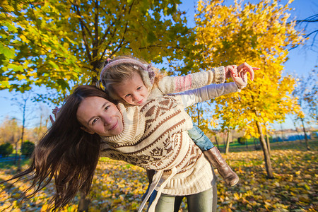 可爱女孩和快乐母亲的肖像在温暖的阳光明媚的日子里在黄色的秋天森林里玩得开心