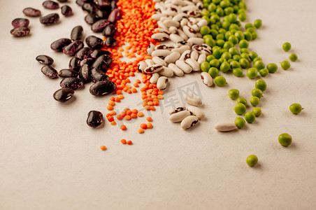 各种干豆类的集合，排列成一条水平线，顺序混乱：红扁豆、绿豌豆、红豆、白豆特写在白色背景上。