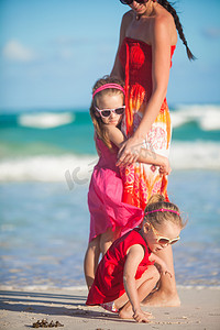 阳光明媚的日子里，年轻妈妈和两个可爱的女儿在异国情调的海滩散步