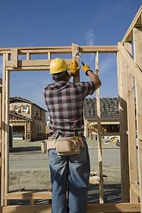 一名建筑工人在现场的木框架上敲钉子的后视图