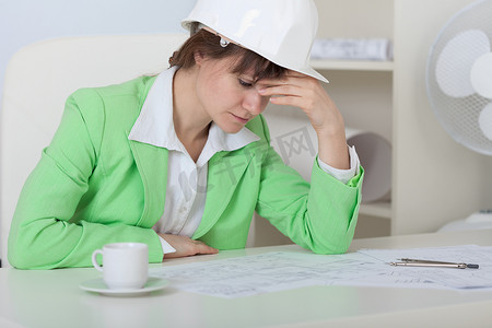 疲惫的女人 — 戴头盔的工程师坐在办公室的桌子旁