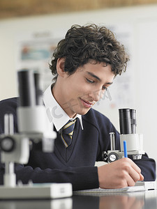 男学生在实验室里用显微镜记下一些东西