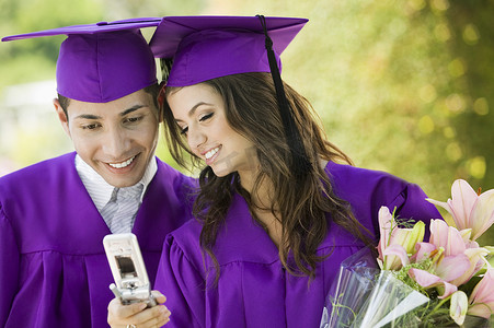 快乐的男女毕业生在户外看手机
