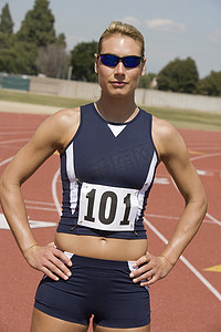 自信的女运动员穿着运动服，双手叉腰在跑道上