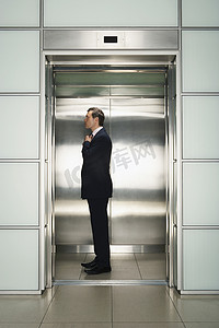 电梯里摄影照片_中年商人在电梯里调整领带准备面试的侧面照片