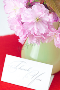 花瓶里的樱花和一张在红色背景上签名的感谢卡