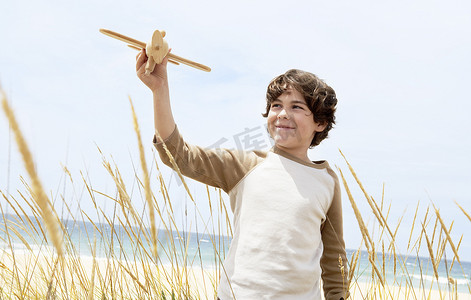 举手小男孩摄影照片_快乐可爱的小男孩在海滩上的植物中飞行玩具飞机