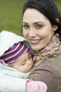 在公园里抱着睡着的婴儿的快乐年轻女人的特写