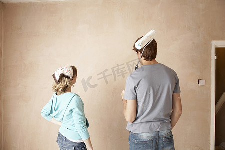家装电商首页摄影照片_在未装修的房间里用油漆滚筒看墙的夫妇的后视图