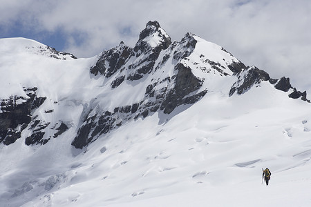 徒步旅行者在雪中走向远方山峰的后视图