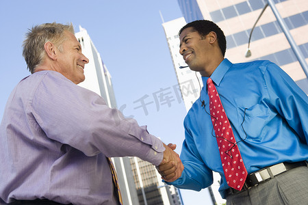 两个快乐的商人为成功交易握手的低视角