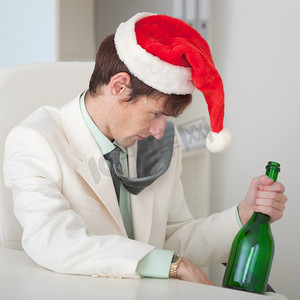 戴着圣诞帽、带瓶子的醉汉坐在桌边
