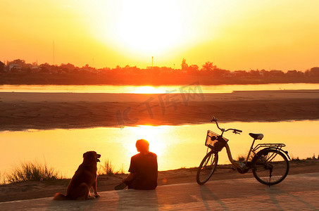 剪影男人带着狗在湄公河水边看日落