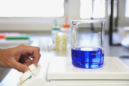 人手分析装满蓝色液体的科学玻璃容器