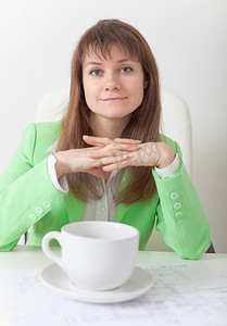 年轻女人坐在桌旁，端着大杯咖啡