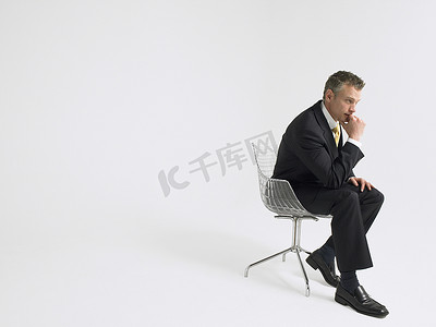 灰色背景下坐在椅子上的一位体贴的商人的全长