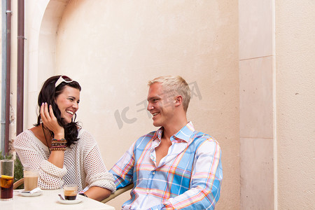 快乐的年轻夫妇坐在咖啡馆餐厅外喝咖啡