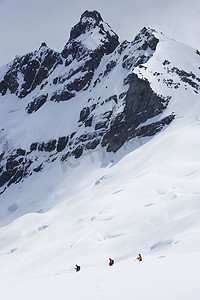团队规模摄影照片_三名远足者在雪中前往远峰的远侧视图