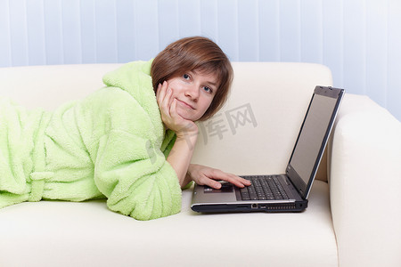 穿着绿色晨衣的年轻女孩在沙发上用电脑