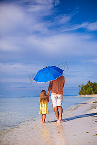 走在一把蓝色伞下的年轻父亲和他的小女儿的后视图