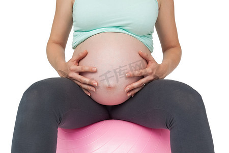坐在粉红色运动球上的孕妇拿着她的肿块