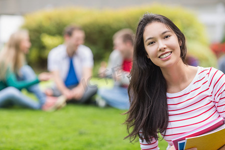 女人坐着摄影照片_在公园里微笑的大学生和模糊的朋友