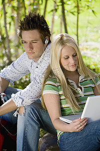 在大学校园里，年轻男子听音乐，而女性则使用笔记本电脑