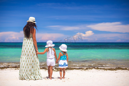阳光明媚的日子里，时尚年轻母亲和她的两个孩子在异国情调的海滩上的后视