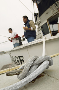 特写一根绑在夹板上的绳子，背景是钓鱼的人