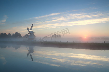 在有薄雾的日出期间河边的荷兰风车